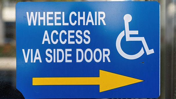 Hinweisschild für Rollstuhlfahrer mit Pfeil auf eine Seitentür an einem Schaufenster der Stadt - Foto, Bild