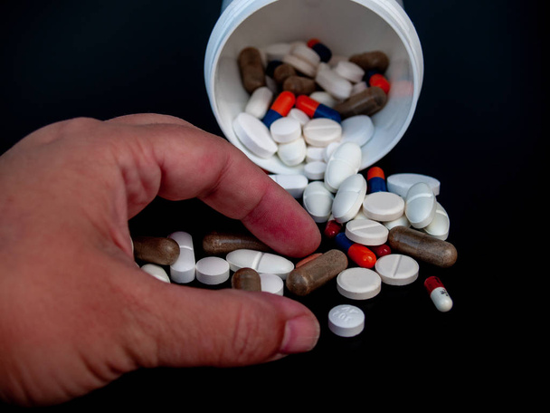 Una persona sosteniendo píldoras de diferentes tamaños, formas y colores con su mano. Concepto de salud
 - Foto, Imagen