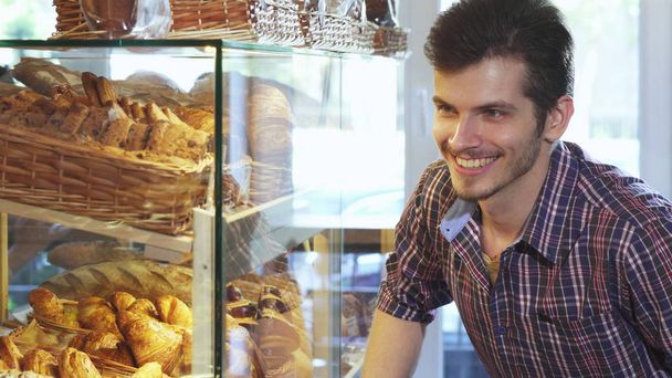 ハンサムな男がパン屋でショーケースからデザートを選択 - 写真・画像