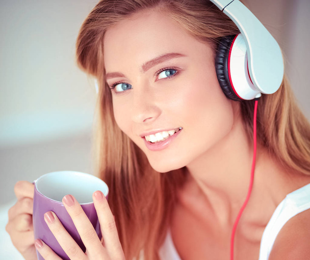 Portrait of beautiful woman in morning listening music sitting on bed at home - Foto, Imagen