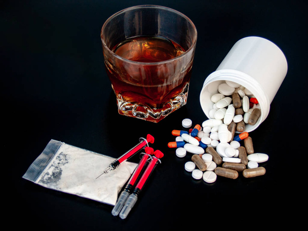 Comprimidos de diferentes tamanhos, formas e cores, um copo de uísque, drogas e seringas Conceito de drogas e álcool
 - Foto, Imagem