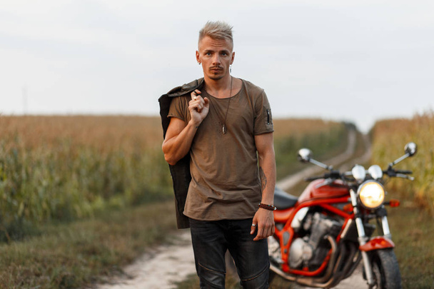 グリーンの t シャツとトウモロコシ畑では自然のオートバイに近い黒パンツ カーキ ジャケットのハンサムな流行に敏感な男 - 写真・画像