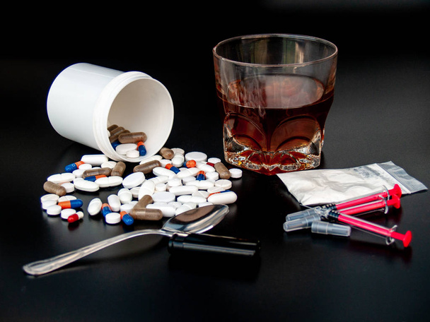 Pillen van verschillende maten, vormen en kleuren, een glas whisky, drugs en spuiten Concept van drugs en alcohol - Foto, afbeelding