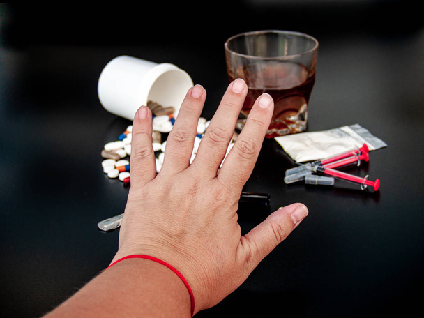 Een persoon die gebaren met zijn hand stop drugs, pillen van verschillende maten, vormen en kleuren, een glas whisky, drugs en spuiten Concept van drugs en alcohol - Foto, afbeelding
