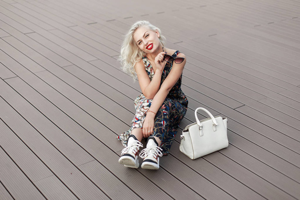 Забавная красивая молодая модель с красными губами в винтажной палитре с узором из модных туфель, сидящая на деревянном полу. Женский стильный белый мешок
  - Фото, изображение