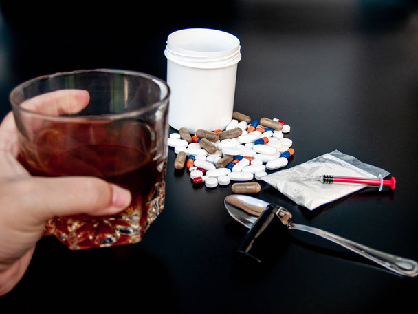 Een persoon met een glas whiskey aan hun kant. Pillen van verschillende maten, vormen en kleuren, medicijnen en spuiten Concept van drugs en alcohol - Foto, afbeelding