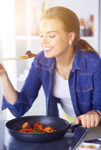 Young woman cooking healthy food holding a pan with vegetables is it. Healthy lifestyle, cooking at home concept - Foto, Imagen