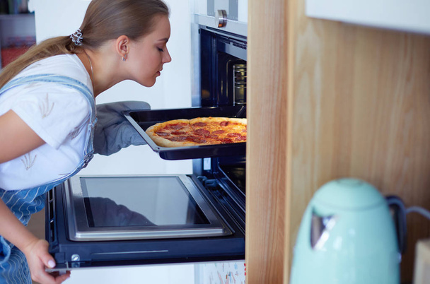Happy young woman cooking pizza at home - Фото, изображение