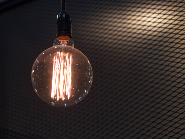 Вольфрамова помаранчева лампа, що звисає всередині будівлі з чорним залізним парканом навколо, Освітлення в будівлях з різнокольоровими електричними лампами, м'який фокус
. - Фото, зображення