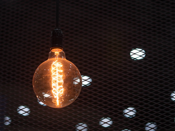 Вольфрам оранжевый лампочка висит на внутренней стороне здания с черным железным забором вокруг, освещение в зданиях с разноцветными электрическими лампами, мягкий фокус
. - Фото, изображение
