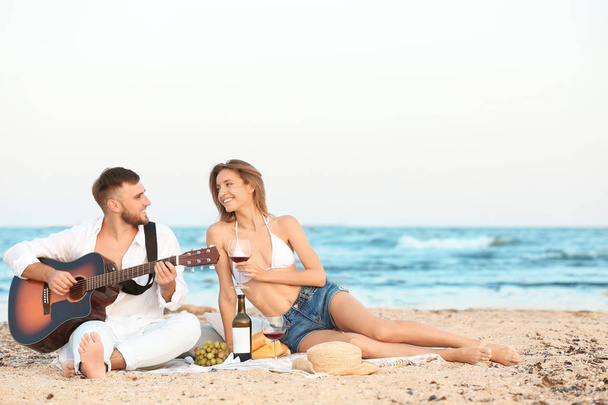 Young couple with guitar having romantic dinner on beach - Fotoğraf, Görsel