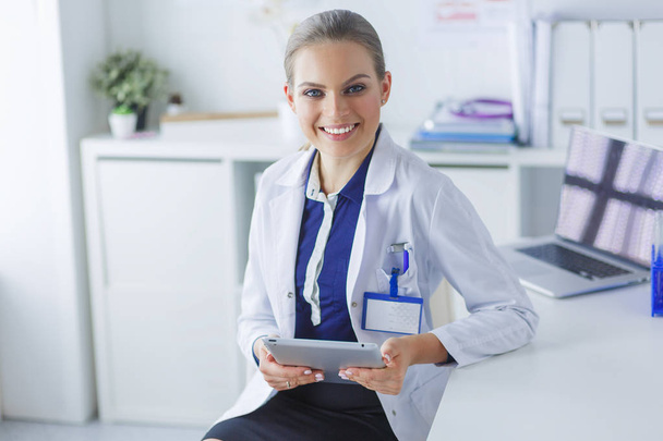 Portrait of woman doctor at hospital corridor, holding tablet computer, looking at camera, smiling - Фото, изображение