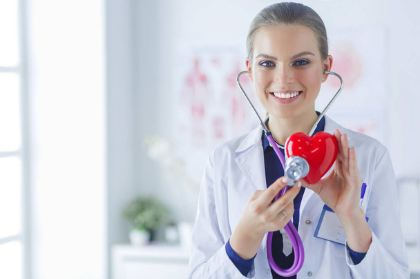A doctor with stethoscope examining red heart, isolated on white background - Фото, изображение