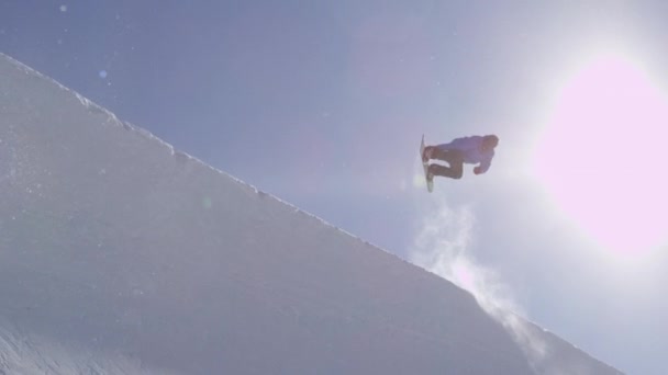 スローモーション: 若いプロスノーボーダー大きな山スノーパークで半分の管に乗って、ハーフパイプの壁と太陽の上をジャンプ、晴れた冬のトリックやグラブの回転を実行します。 - 映像、動画