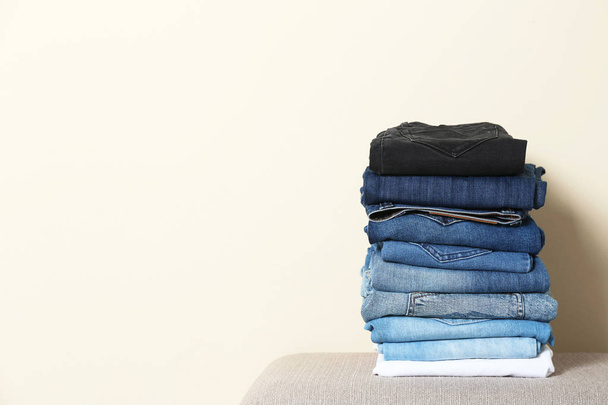 Stack of different jeans on ottoman against light background. Space for text - Фото, зображення