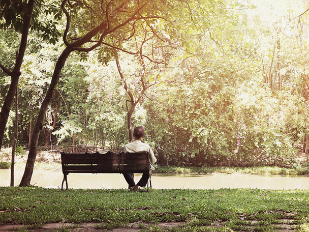 Widok z tyłu z samotny stary człowiek siiting na drewnianej ławce w parku publicznego o wschodzie słońca. Efekt filtra Vintage. - Zdjęcie, obraz