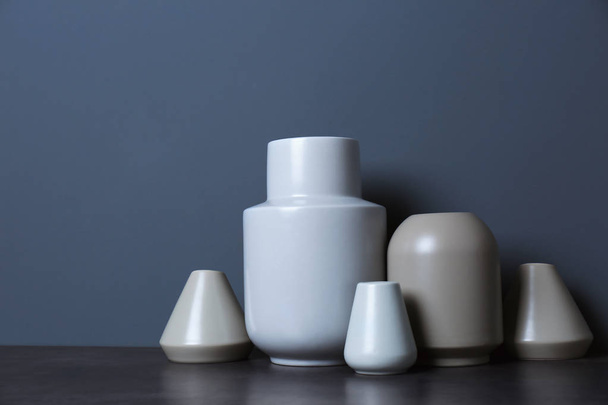 Beautiful ceramic vases on table against color wall with space for text - 写真・画像