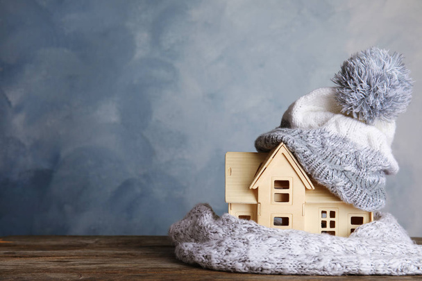 Plywood toy house with warm hat, scarf and space for text against color background. Heating system - Foto, Imagem