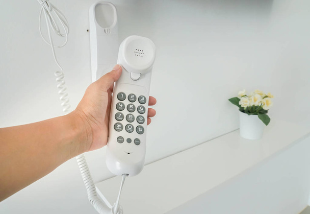 Detailní záběr žena držet sluchátko s numerickou klávesnicí telefonu pevné zdi levé ruky pro volání. - Fotografie, Obrázek