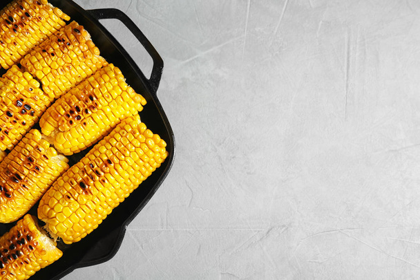 Fresh grilled tasty corn cobs in pan and space for text on light background, top view - Fotó, kép
