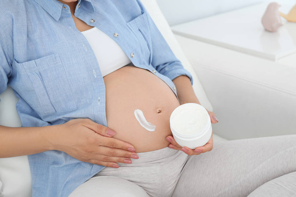 Pregnant woman applying body cream on belly at home, closeup - Foto, Imagem