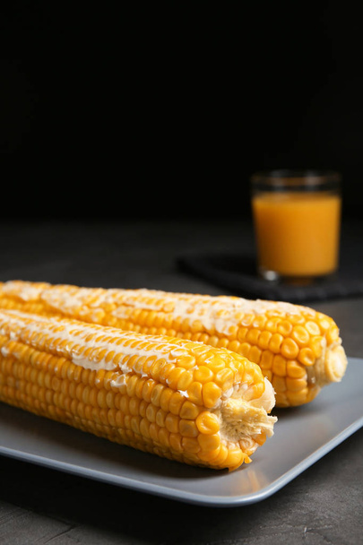Delicious boiled corn cobs with butter on gray table against black background. Space for text - Fotó, kép