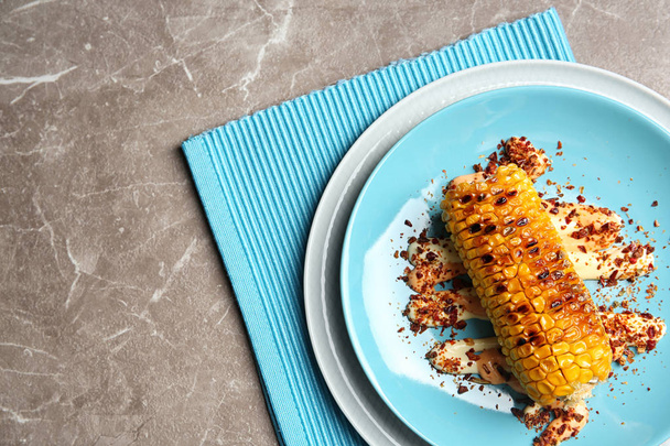 Plate with delicious grilled corn cob and spices on table, top view - Fotó, kép