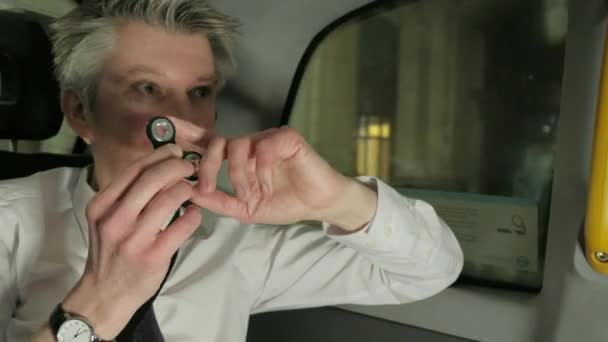 Caucasian businessman playing with a fidget spinner in the back of a taxi cab at night - Footage, Video