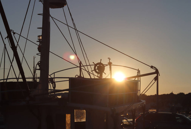 Stuurwiel op de brug van een vissersboot afgemeerd in een jachthaven. Panorama van de avond-zonsondergang in de haven van de mediterrane toeristische stad. - Foto, afbeelding