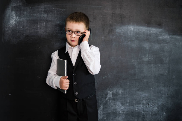 Young boy's standing with phone and notebook in his hands near blackboard. Young businessman. Creative design concept for 2019 calendar - Φωτογραφία, εικόνα
