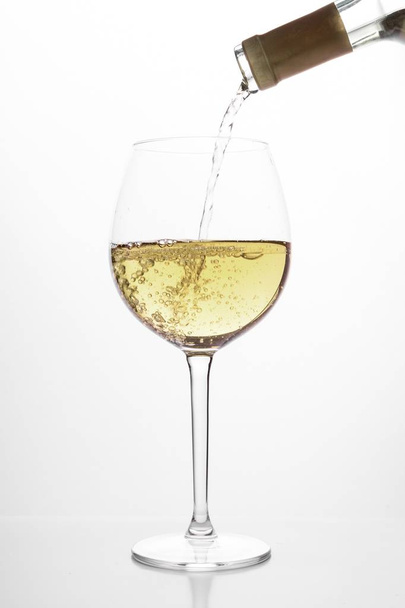 pouring white wine into glass, on white background - Фото, зображення