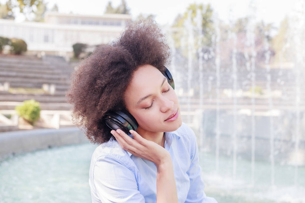 Porträt der schönen gemischten Rasse junge Frau, die Musik mit drahtlosem Kopfhörer im Freien hört - Foto, Bild
