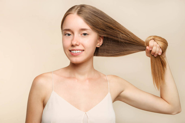 Girl with long blond hair on beige background. Concept hair care. - 写真・画像