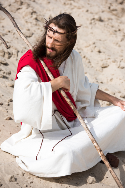 İsa elbise içinde kırmızı kuşak ve lotus pozisyonda oturan dikenli taç çöl ve seyir içinde kum uzak - Fotoğraf, Görsel