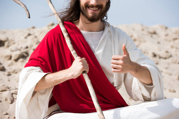 levágott kép Jézus, ült a lótusz helyzet, a homok, a betöltő személyzet és a hüvelykujj felbukkan a sivatagban - Fotó, kép