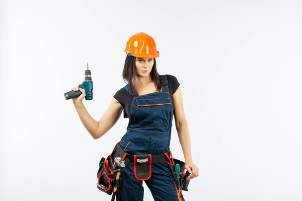 Young woman with toolbelt using driil and some power tools for her work at home. Girl working at flat remodeling on white background. Building, repair and renovation. - Photo, Image