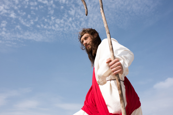 vue en angle bas de Jésus en robe, ceinture rouge et couronne d'épines debout avec le bâton contre le ciel nuageux
 - Photo, image