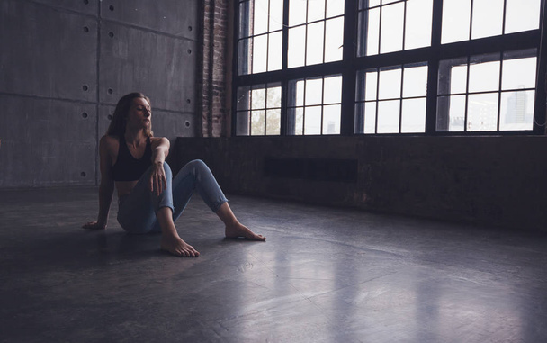 young beautiful woman dancer contemporary in tops and jeans sits on the floor in dance studio - Фото, зображення