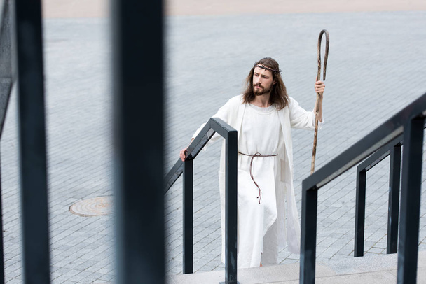 high angle view of Jesus in robe and crown of thorns walking on stairs with staff - Photo, image