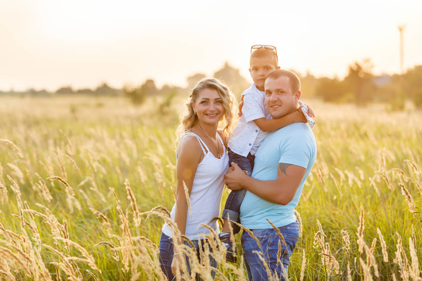 Giovane famiglia con figlio che cammina e si diverte nel campo verde al tramonto
 - Foto, immagini