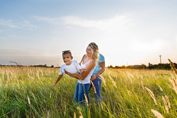 Familia joven con hijo caminando y pasando un buen rato en el campo verde al atardecer
 - Foto, imagen