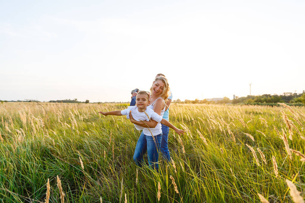 Молодая семья с сыном гуляет и хорошо проводит время в зеленом поле на закате
 - Фото, изображение