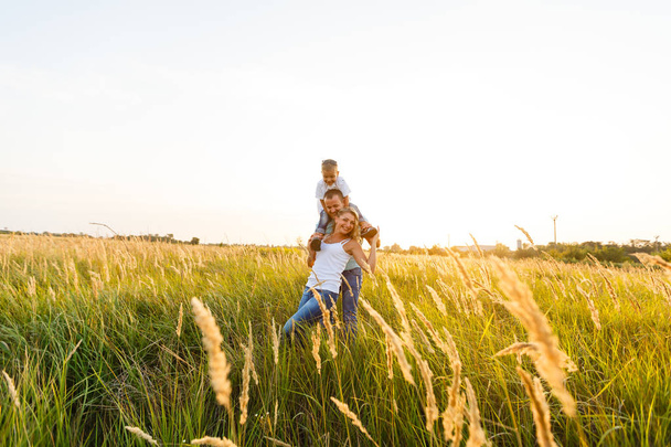 Fiatal család fia, gyaloglás és birtoklás jó idő, zöld mezőben naplementekor - Fotó, kép