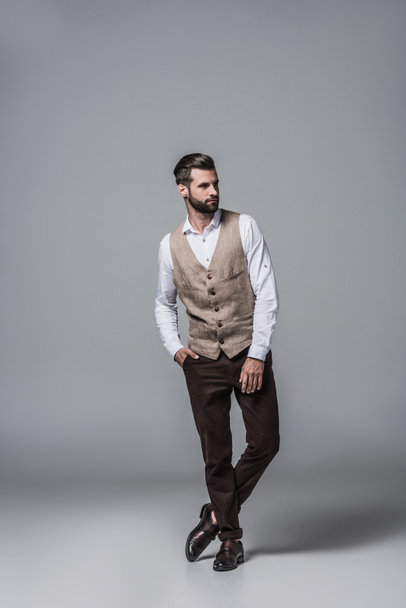 handsome bearded man posing in elegant stylish waistcoat on grey - Fotó, kép