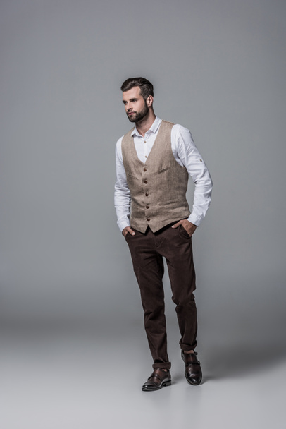 handsome bearded man posing in trendy elegant waistcoat on grey - Zdjęcie, obraz
