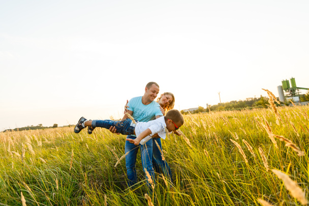 Giovane famiglia con figlio che cammina e si diverte nel campo verde al tramonto
 - Foto, immagini
