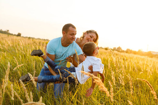 Młode rodziny z synem spaceru i dobra zabawę w zielony pole o zachodzie słońca - Zdjęcie, obraz