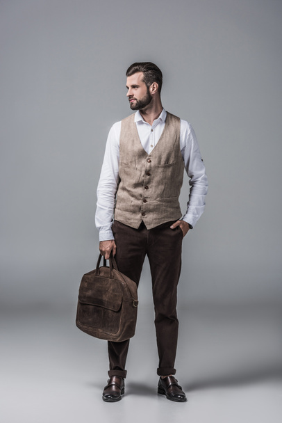 stylish elegant man in waistcoat posing with leather bag on grey - Photo, Image