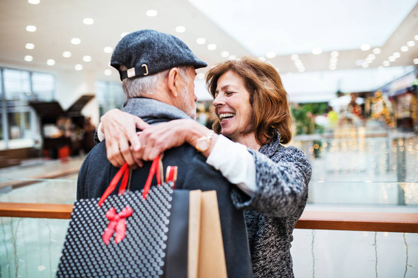 Щаслива старша пара з паперовими пакетами в торговому центрі, обіймаючи
. - Фото, зображення
