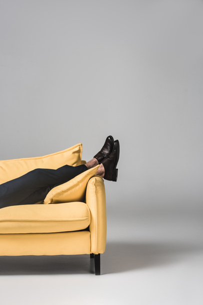 vista recortada de piernas masculinas tumbadas en sofá amarillo sobre gris
 - Foto, Imagen